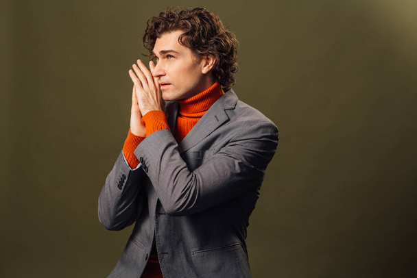 Full lengh portrait of a tall handsome man dressed in orange turtleneck, grey jacket and white jeans posing on the green background - Foto, Imagem