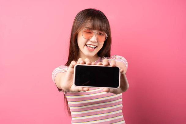 Изображение молодой азиатской девушки в розовой футболке на розовом фоне - Фото, изображение