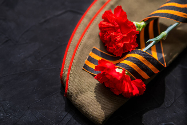 Victory Day holiday. holiday card with A St. George ribbon, flowers and military cap. Dark Background on May 9, copy space - Photo, Image