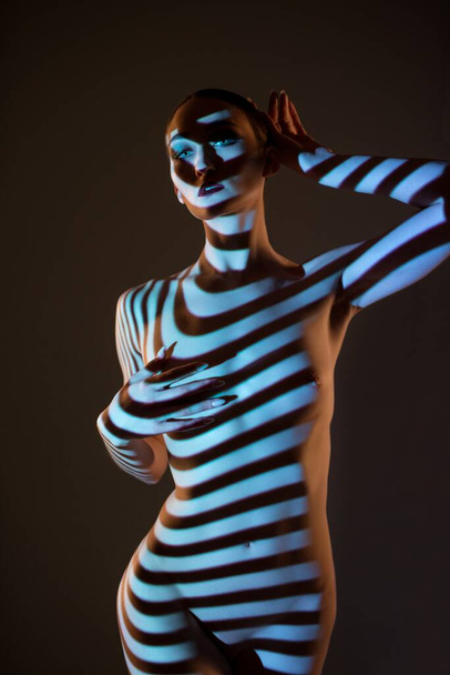Nude woman standing in dark studio with striped illumination - Фото, зображення
