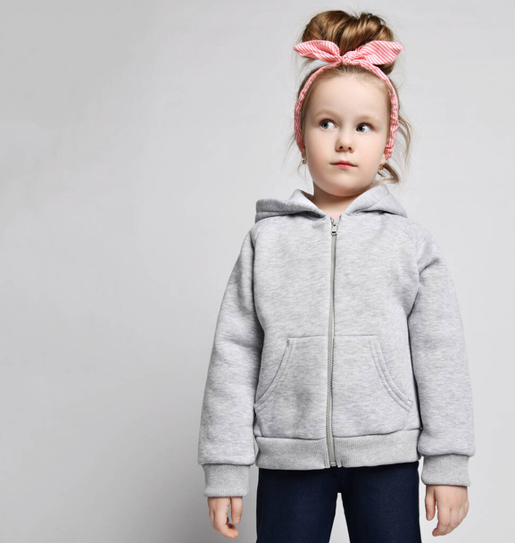 Portré egy szőke lányról szürke kapucnis pulcsiban, cipzárral és zsebekkel, aki még mindig félrenéz a fénymásolótérre. - Fotó, kép