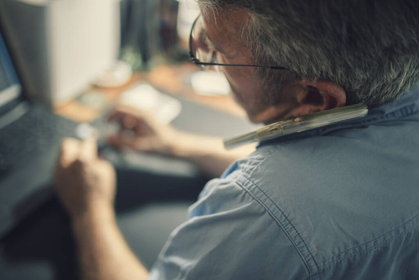 Ein älterer Mann sitzt an einem Schreibtisch vor einem Laptop - Foto, Bild