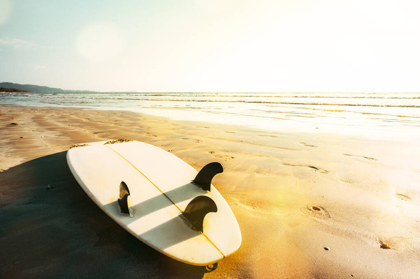 Deska surfingowa na plaży o zachodzie słońca. Pejzaż morski letniej plaży z morzem i błękitnym tle nieba. - Zdjęcie, obraz
