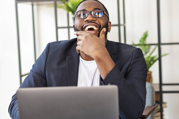 Happy successful African American young male freelancer or manager sitting at a desk in the office; rejoicing in a successful deal or new business project - Foto, Bild