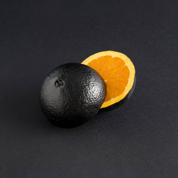 Creative summer composition with sliced black metallic orange fruit on black background. Minimal retro futuristic or space fruit concept. - Foto, Imagen