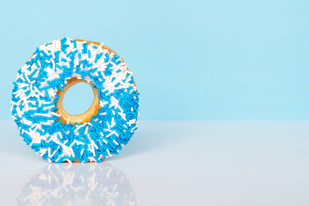 Donut with blue and white sprinkles on blue background with reflection and copy space for text. - Photo, Image