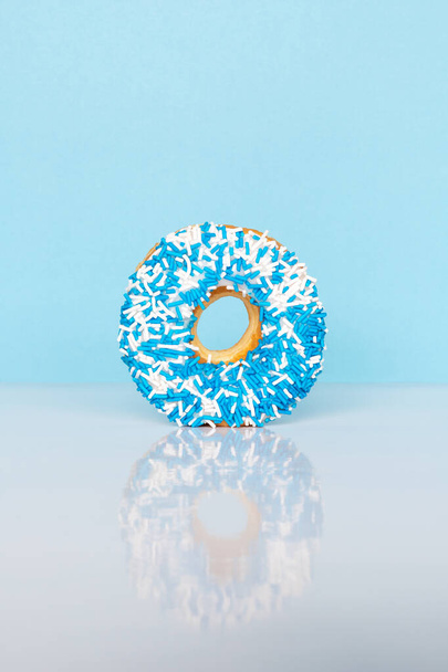 Donut con salpicaduras azules y blancas sobre fondo azul con espacio de reflexión y copia para texto. - Foto, Imagen