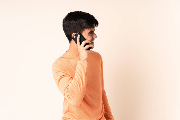 Beau homme sur fond beige isolé gardant une conversation avec le téléphone portable avec quelqu'un - Photo, image