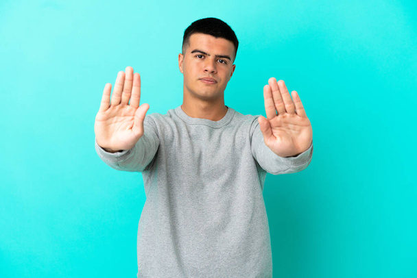 Jonge knappe man over geïsoleerde blauwe achtergrond maken stop gebaar en teleurgesteld - Foto, afbeelding