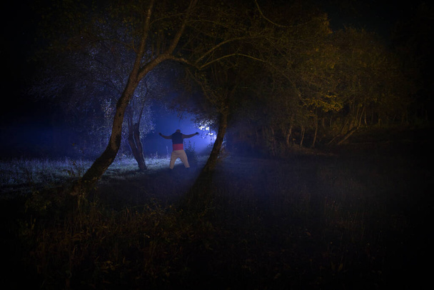 Silhouette einer Person, die im dunklen Wald mit Licht steht. Horror-Halloween-Konzept. Seltsame Silhouette in einem dunklen Gruselwald bei Nacht - Foto, Bild