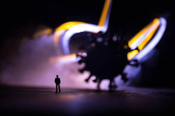 Globální pandemický koncept viru korony. Miniaturní muž stojící poblíž velkého románu Corona virus ve tmě. Kreativní dekorace s mlhou a podsvícením. Selektivní zaměření - Fotografie, Obrázek