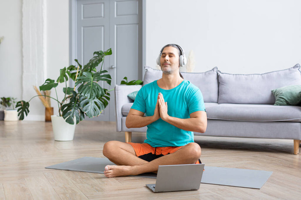 Meditating at home - using from the internet to monitor the workout. He listens to relaxing meditation music through headphones. - Foto, Imagem