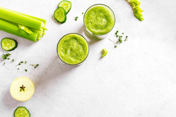 Green vegetable juice or smoothie in glasses. Fresh squeezed detox green juice and bunch of organic celery, cucumber, apple on white table, copy space. - Фото, изображение