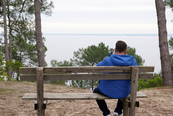 mężczyzna tylny widok z powrotem siedzieć na drewnianej ławce oglądać plaża woda jezioro sam - Zdjęcie, obraz