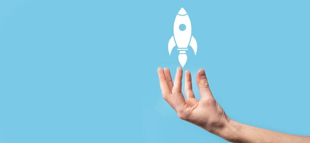 男性の手は離陸ロケットアイコンを保持し、青の背景に打ち上げます。ロケットが打ち上げられ、飛んでいる、ビジネスは、現代の仮想インターフェイス上のアイコンマーケティングを起動します。 - 写真・画像
