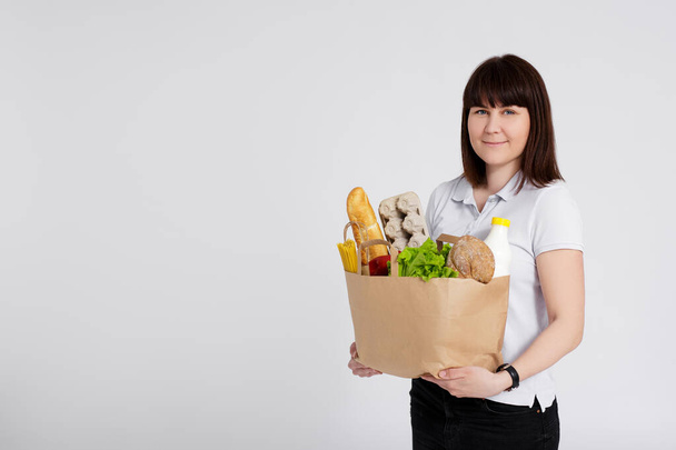 портрет молодой женщины с бумажным пакетом, полным продуктов на белом фоне с копировальным пространством - Фото, изображение