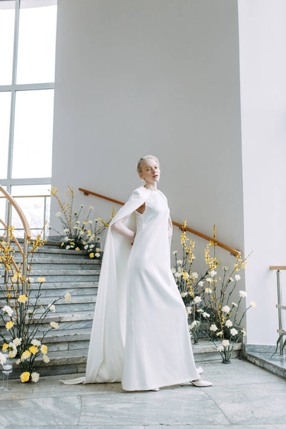 Modern floristics in yellow shades. Fashionable image of the bride. A trendy bride in a white dress on the stairs in a bright interior. - Φωτογραφία, εικόνα
