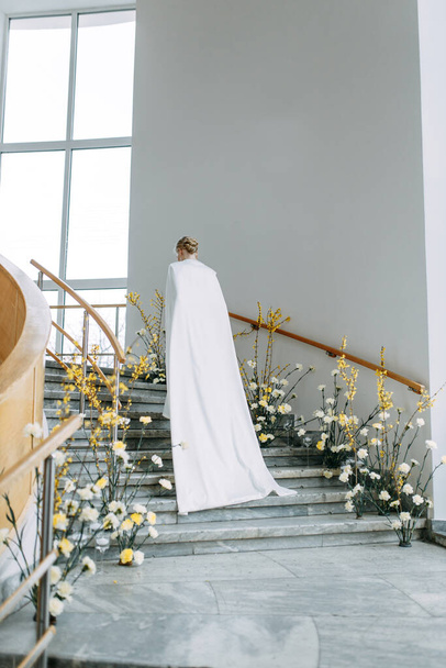 Modern floristics in yellow shades. Fashionable image of the bride. A trendy bride in a white dress on the stairs in a bright interior. - Foto, immagini