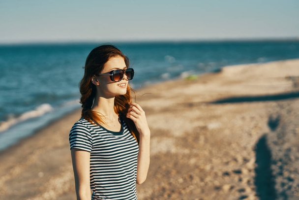 piękna kobieta w t-shircie i okularach na plaży w pobliżu morza w górach - Zdjęcie, obraz