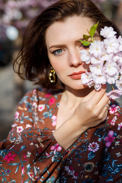 Portrét roztomilé a krásné ženy dívka v šatech v zahradě uprostřed kvetoucí sakura. jaro a slunce. Rozmazané pozadí a vybrané zaměření. - Fotografie, Obrázek