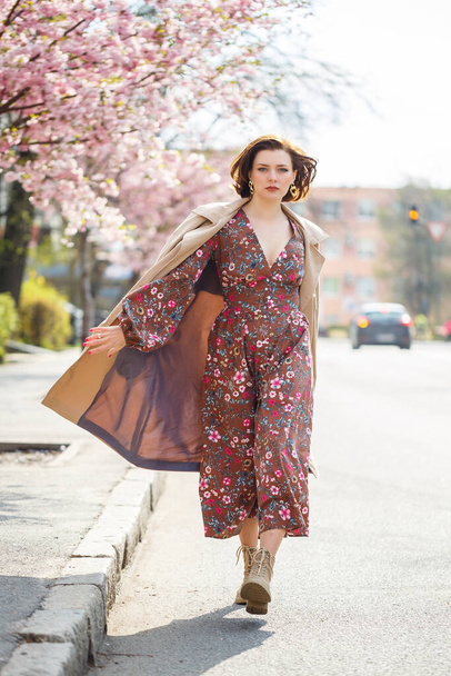 In the spring, a woman walks along a blooming street with sakura trees. A girl in a long silk elegant vintage dress walks among the flowering trees - Fotó, kép