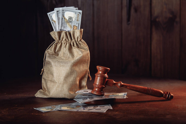 Money bag with dollar banknotes and judges gavel. Litigation, dispute resolution, conflict of interest settlement - Фото, изображение