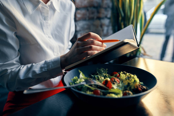 notepad with a pen in hand and salad in a plate restaurant cafe inscription - Foto, Bild
