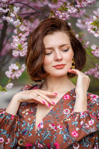 女性が春の通りを歩いている。女の子は花の木の香りを楽しんでいます。桜の咲くドレスを着た美しい女性 - 写真・画像
