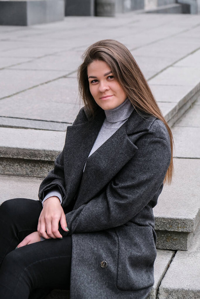 Portrait of young smiling caucasian brunette woman. Businesswoman outdoors in business downtown. Urban city street lifestyle. Long coat and hair. - Photo, image