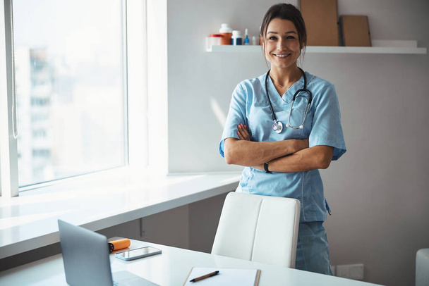 Cheerful female doctor standing by the table in clinic - Photo, image