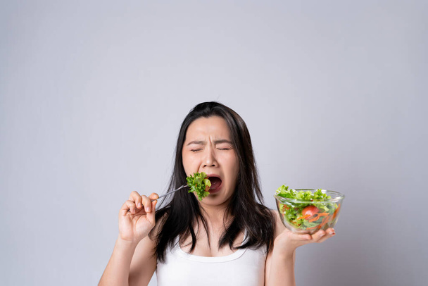 Ασιάτισσα που προσπαθεί να φάει σαλάτα για δίαιτα απομονωμένη σε λευκό φόντο. Υγιεινός τρόπος ζωής με καθαρή έννοια τροφίμων. - Φωτογραφία, εικόνα
