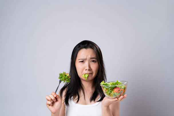 Ασιάτισσα που προσπαθεί να φάει σαλάτα για δίαιτα απομονωμένη σε λευκό φόντο. Υγιεινός τρόπος ζωής με καθαρή έννοια τροφίμων. - Φωτογραφία, εικόνα