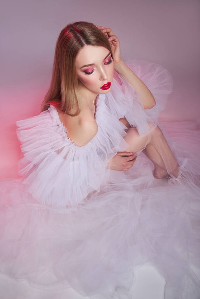 Beauty Woman bright red makeup. Art nude naked woman in a transparent light dress on a pink background. Professional bright makeup woman - Photo, Image