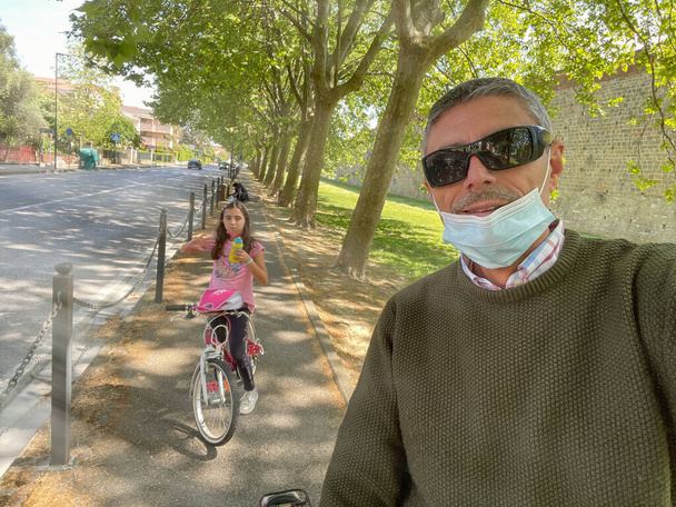 Feliz padre e hija montando una bicicleta al aire libre en la pandemia covid. - Foto, imagen