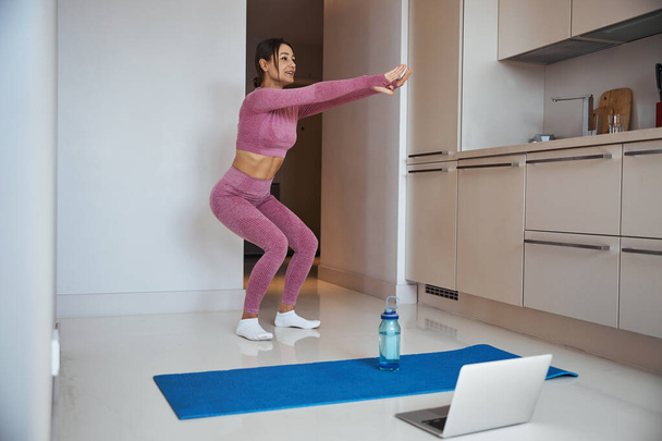 Mujer alegre usando el ordenador portátil y haciendo ejercicio en casa - Foto, imagen