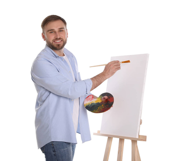 Man painting with brush on easel against white background. Young artist - Photo, image