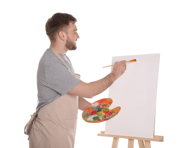 Man painting with brush on easel against white background. Young artist - Foto, Imagem