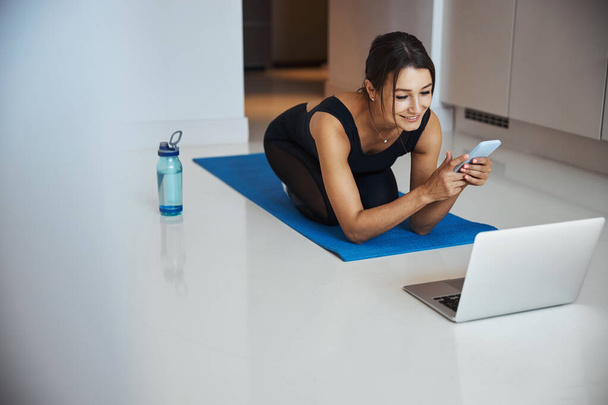 Cheerful sporty woman using cellphone and laptop at home - Photo, Image