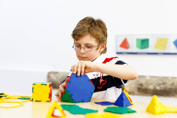 Ευτυχισμένο παιδί αγόρι με γυαλιά που διασκεδάζει με την οικοδόμηση και τη δημιουργία γεωμετρικών μορφών, μαθαίνοντας μαθηματικά και γεωμετρία - Φωτογραφία, εικόνα
