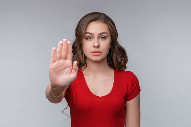 Stop sign, palm on camera, symbol - donT move. Serious young brunette woman shows her palm right on camera. Studio shot, gray background - Foto, imagen