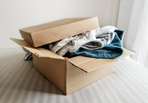 Cardboard box with pre owned clothes inside. Sustainable fashion, resale used clothes - Foto, Imagem