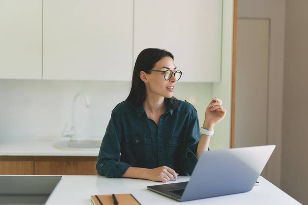 Přední pohled na obchodní žena sedí v moderní bílé kuchyni s notebookem a notebookem - Fotografie, Obrázek