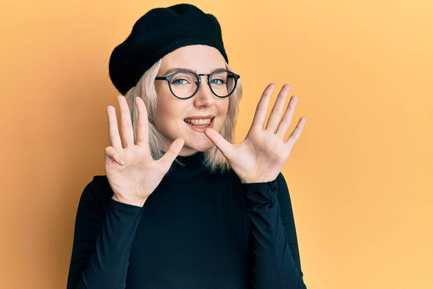 Junge blonde Mädchen im französischen Look mit Baskenmütze zeigt und zeigt mit den Fingern Nummer neun, während sie selbstbewusst und glücklich lächelt.  - Foto, Bild