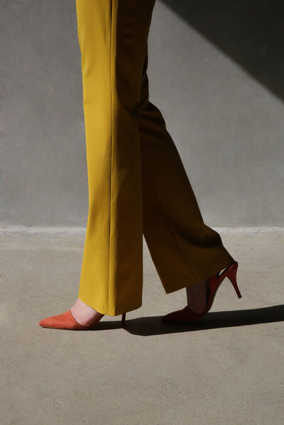 Fashionable young woman in yellow tailored trousers and orange heels. - Photo, Image