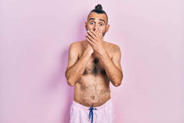 Un joven hispano sin camisa usando traje de baño sorprendió cubriendo la boca con las manos por error. concepto secreto.  - Foto, imagen