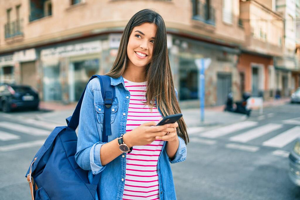 Nuori latino opiskelija tyttö hymyilee onnellinen käyttäen älypuhelin kaupungin. - Valokuva, kuva