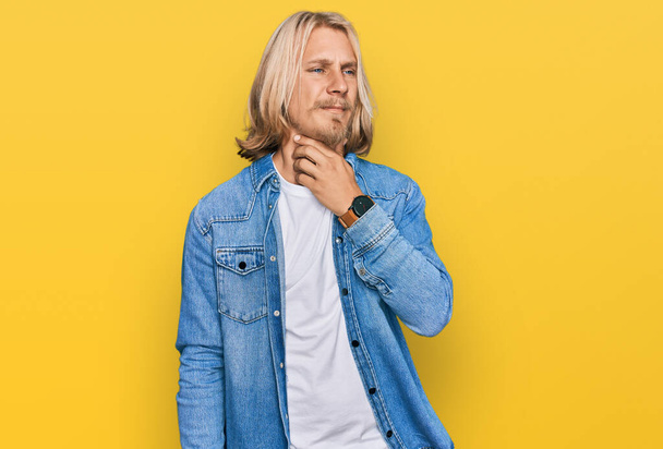 Caucasian man with blond long hair wearing casual denim jacket touching painful neck, sore throat for flu, clod and infection  - Photo, Image