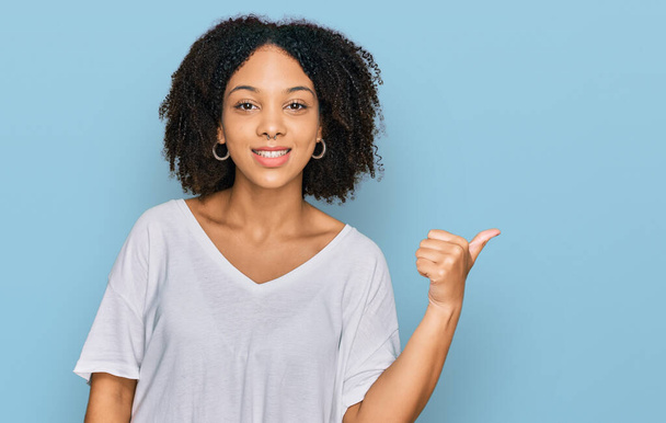 Молода афроамериканська дівчина в повсякденному одязі посміхається з щасливим обличчям і вказує на бік з великим пальцем вгору.  - Фото, зображення