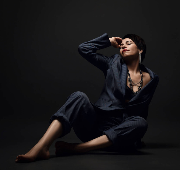 Short haired brunette woman in business smart casual suit on naked body sits on floor with eyes closed and hand at head - Foto, Bild