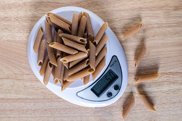 A portion 50 gm of pasta  Penne on a kitchen scales, flat lay - Photo, Image